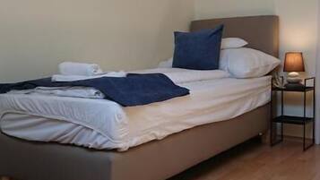 A single bed with a headboard, a bedside table with a lamp, and a wooden floor.