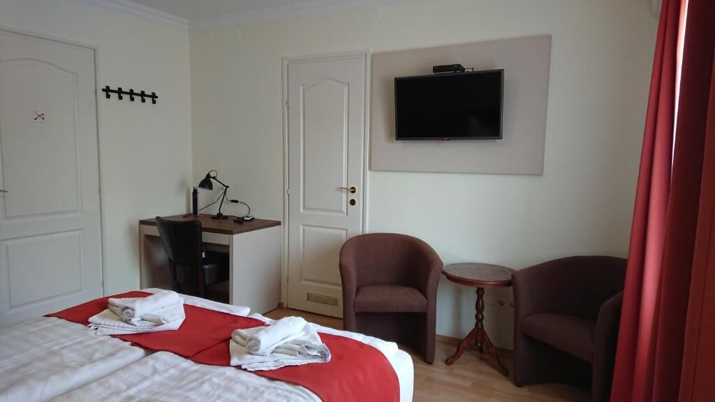 A hotel room with a bed, a desk, a chair, a television, and a small table.