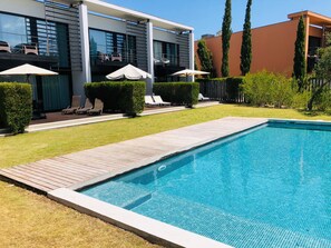 A modern hotel with a swimming pool, lounge chairs, and a well-maintained garden. - Troia Sea and Pool Townhouse (Grandola)