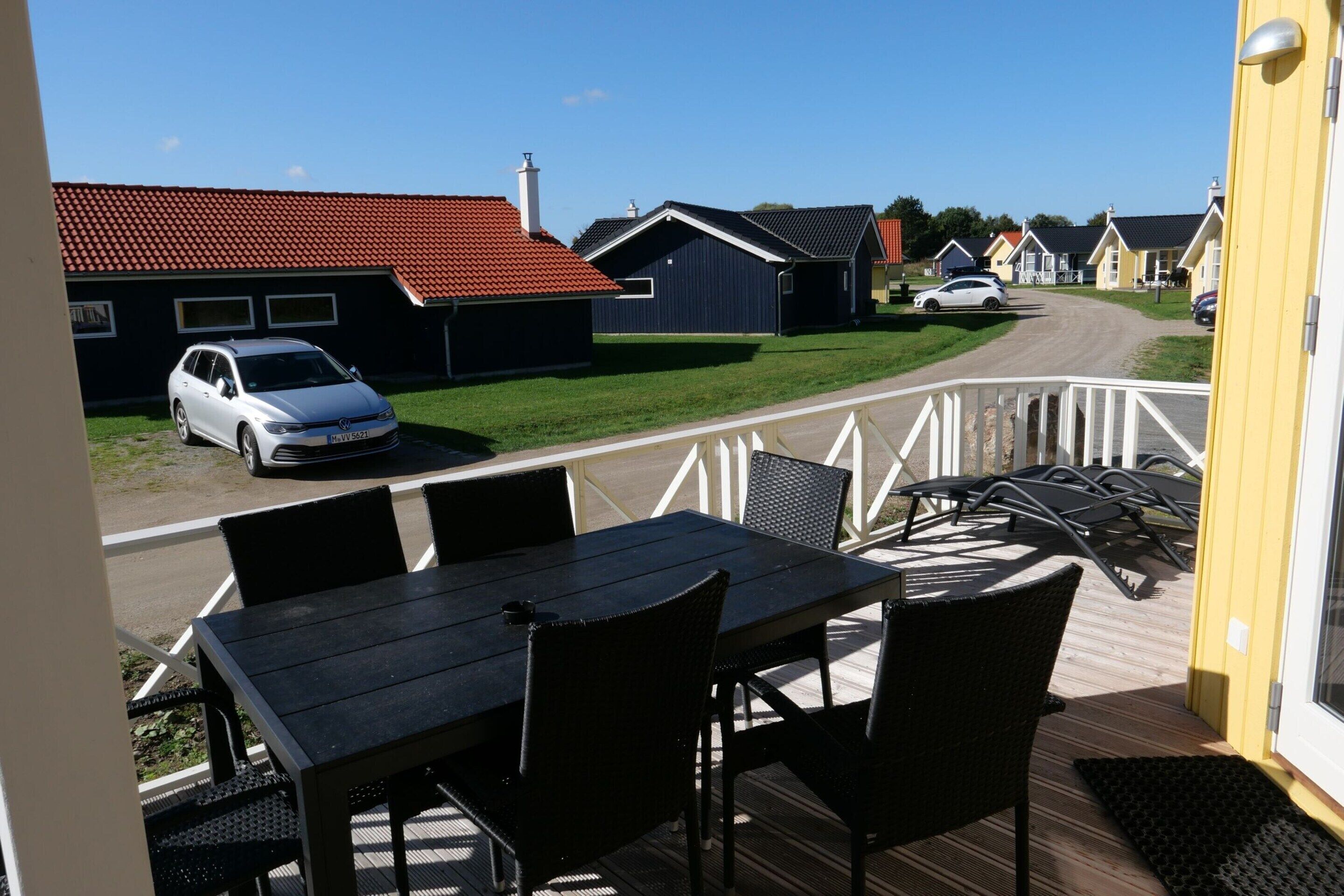 A deck with outdoor furniture, a view of a street with houses, and a parked car.