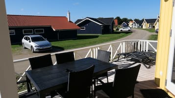 A deck with outdoor furniture, a view of a street with houses, and a parked car.