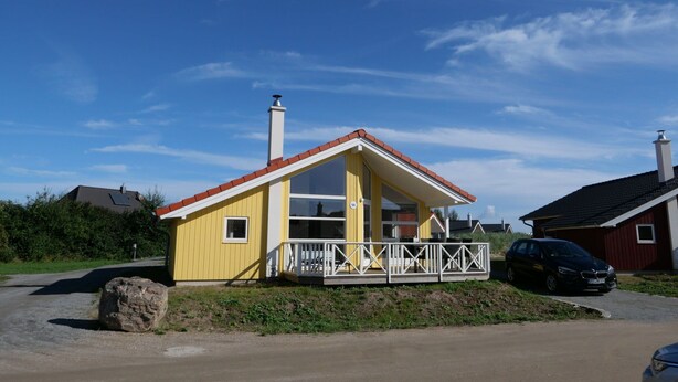 Uma casa amarela térrea com telhado vermelho, varanda branca e chaminé.