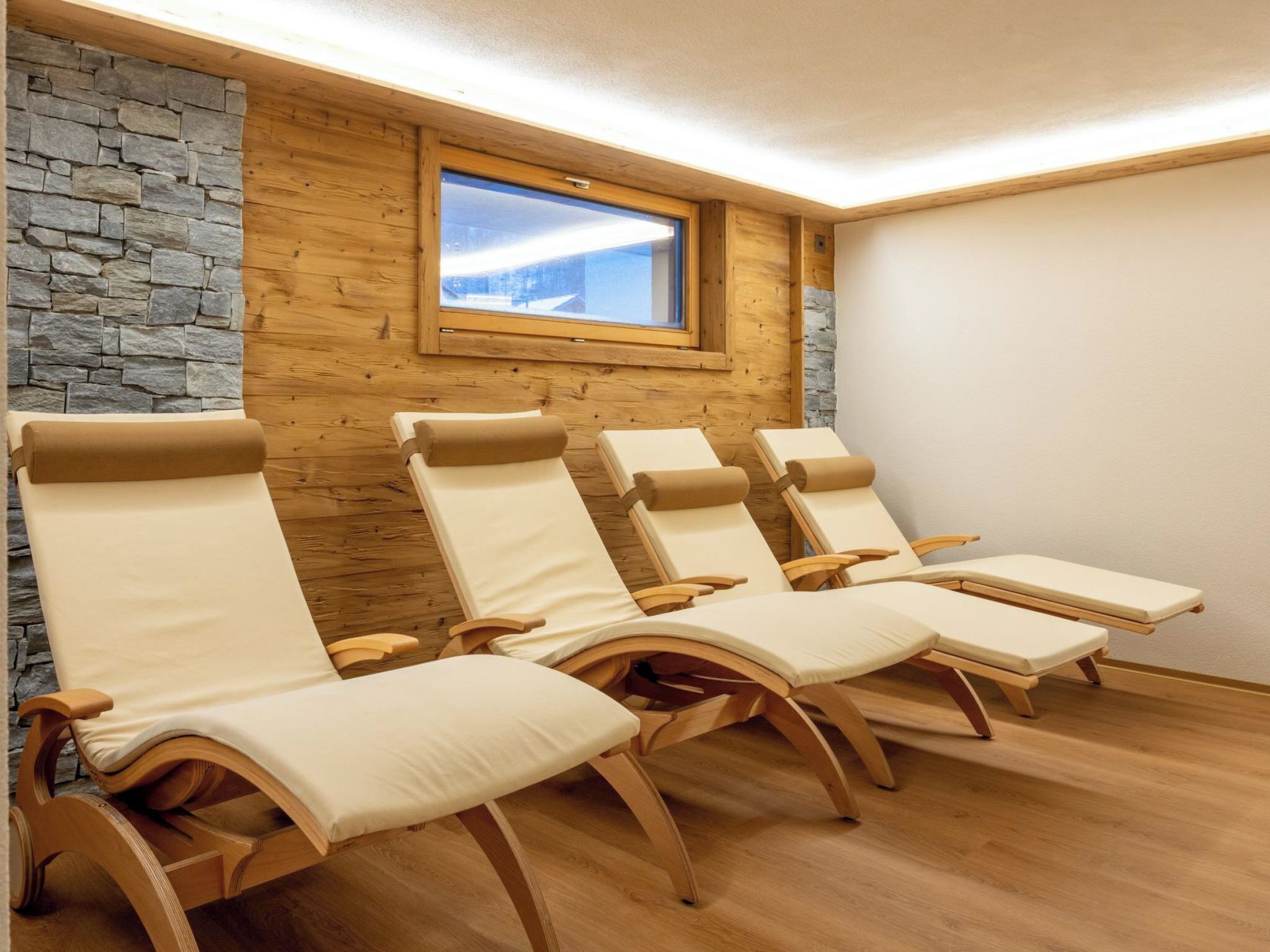 Een kamer met vier houten loungestoelen op een rij, een stenen muur en een raam met uitzicht.