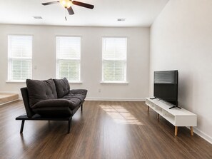 Ein Wohnzimmer mit einem dunkelbraunen Sofa, einer weißen TV-Konsole und einem Deckenventilator.