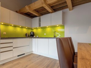Eine moderne Küche mit weißen Schränken, einer grünen Spritzschutzwand und einer Holzbalkendecke.