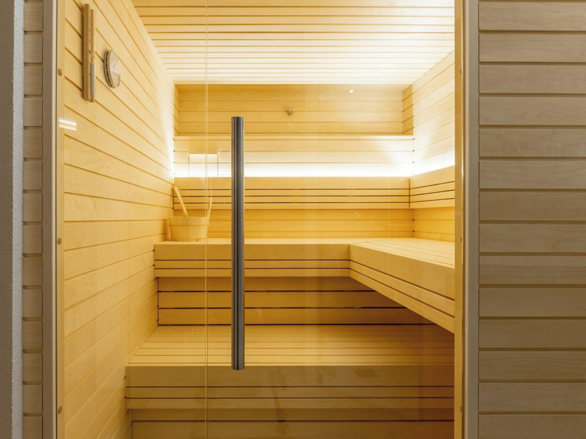 A sauna with wooden walls and benches, a glass door, and a metal handle.