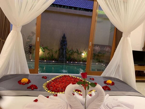 Una cama con dosel, un arreglo floral decorativo y vista a una piscina y una estatua.