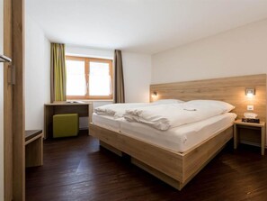 A modern bedroom with a wooden bed, bedside tables, a desk, and a window with curtains. - Haus Alpenrose Appartement/Fewo Alpenrose 4-Bettwohnung 1. OG Ost by Interhome (Saas-Almagell)