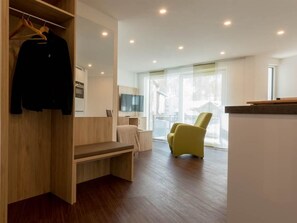 Ein modernes Hotelzimmer mit einer hölzernen Bank, einem gelben Sessel, einem Flachbildfernseher und einem großen Fenster mit Blick ins Freie.
