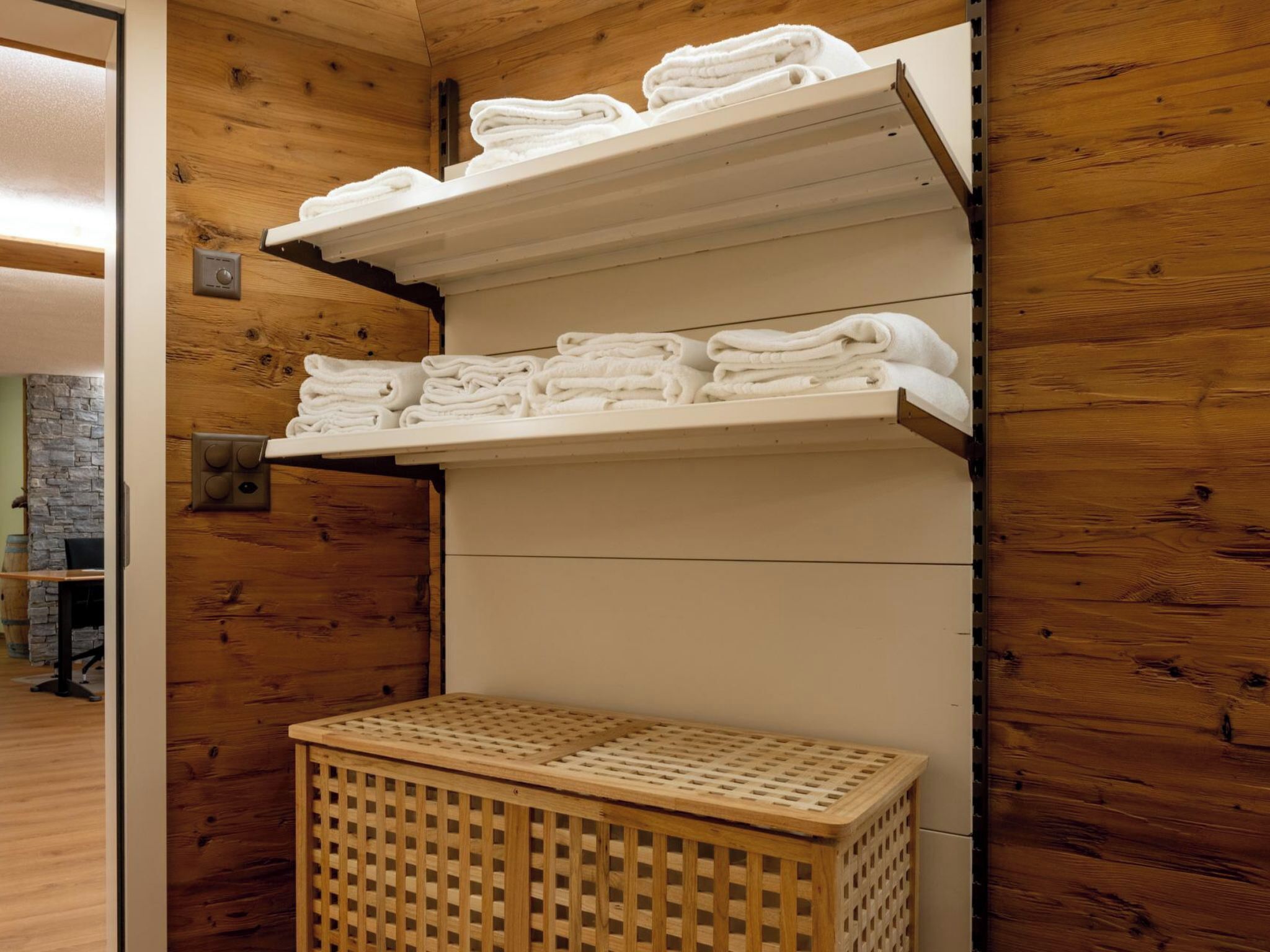 Une salle de bain avec des murs en bois, un banc en bois et des étagères où sont pliés des serviettes.