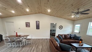 A spacious living area with a high ceiling, a dining table with chairs, a brown leather sofa, and a ceiling fan. - "The Hive" Cottage #1 (Van Buren)