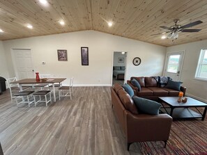 A spacious living area with a high ceiling, a dining table with chairs, a brown leather sofa, and a ceiling fan. - "The Hive" Cottage #1 (Van Buren)