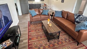 A living room with a brown leather sofa, a coffee table, and a TV. - "The Hive" Cottage #1 (Van Buren)