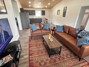 A living room with a brown leather sofa, a coffee table, and a TV. - "The Hive" Cottage #1 (Van Buren)
