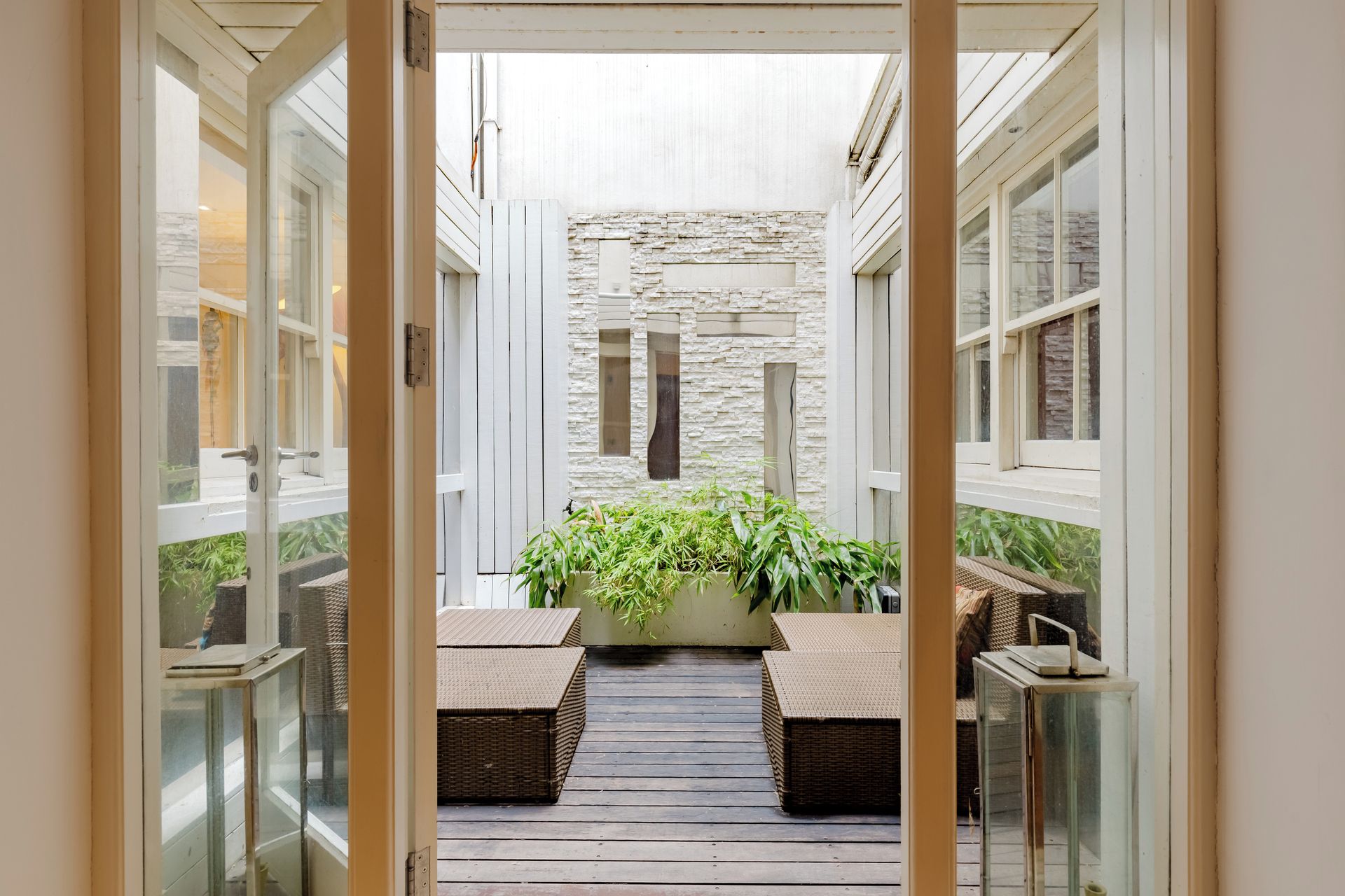 A corridor with a stone wall, two wicker sofas, and a glass door.