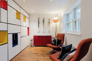 A modern living room with a red sofa, a wooden floor, and a white wall with artwork. - One of a Kind Central London Retreat (Greater London)