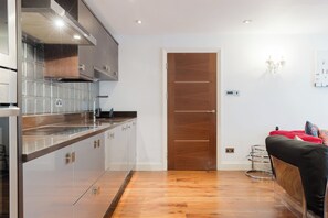 A modern kitchen with a wooden door, a dining area with a red sofa, and a clear view of the adjacent room. - One of a Kind Central London Retreat (Greater London)