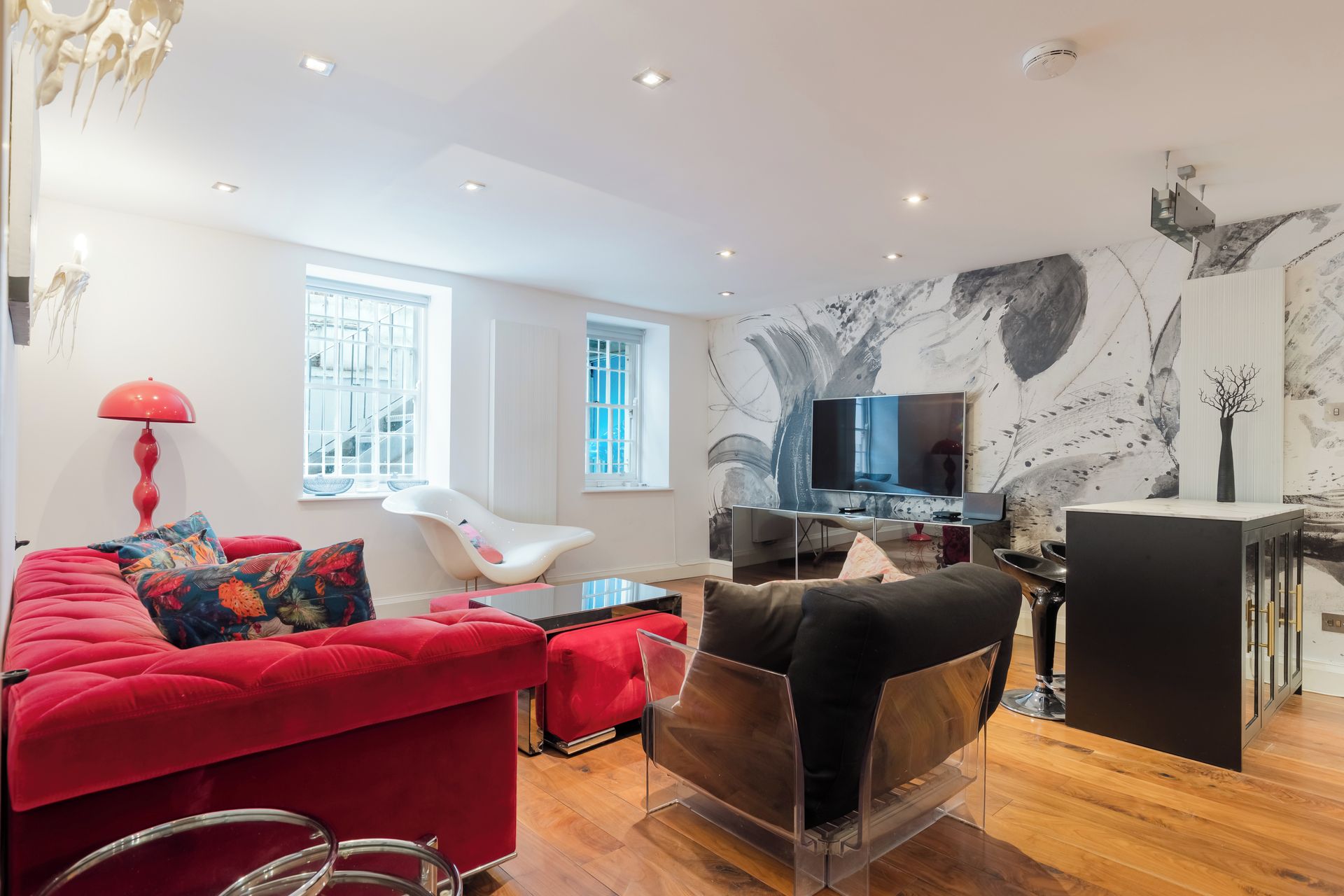 A modern living room with a red sofa, a white chair, a glass coffee table, and a TV.