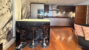 A modern kitchen with a central island, bar stools, and a dining area with a sofa. - Artsy and Spacious 2BDR Flat in Central London (Greater London)