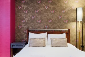 A hotel room with a bed, two pillows, a nightstand, a lamp, and a floral wallpaper. - One of a Kind Central London Retreat (Greater London)