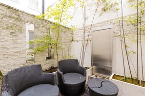 A courtyard with stone walls, a black wicker chair, a small table, and bamboo plants. - One of a Kind Central London Retreat (Greater London)