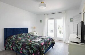 Ein Schlafzimmer mit einem großen Bett, einem Nachttisch mit Lampe, einem Fernseher und einer Schiebeglastür nach draußen.
