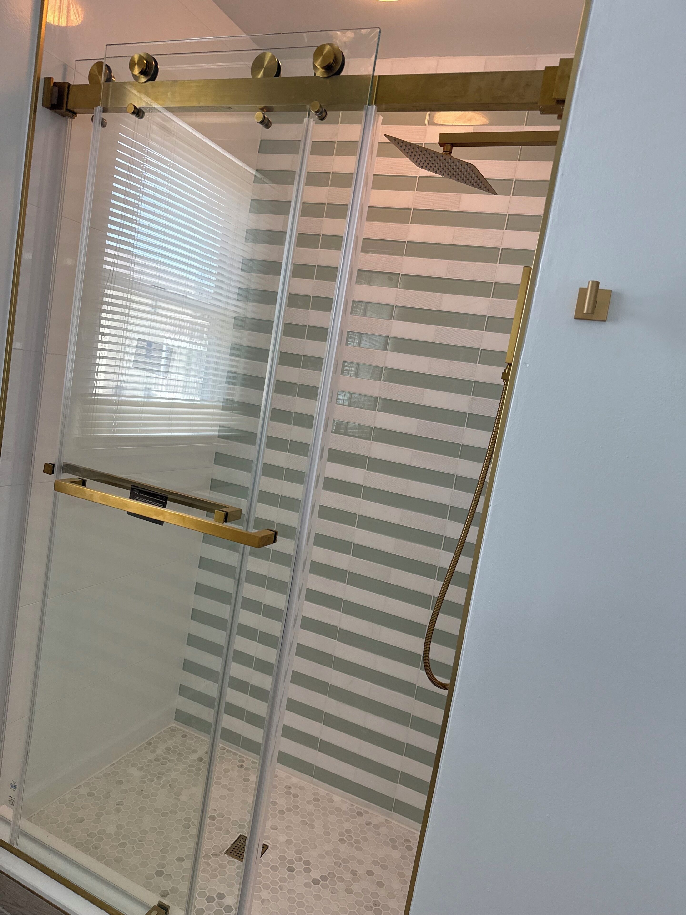 A glass-enclosed shower with a gold handle and a showerhead.