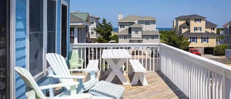 A wooden deck with Adirondack chairs and a picnic table, overlooking a residential area with houses and a clear sky.