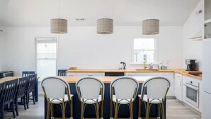 Et moderne køkken med en central ø, barstole, hængende lamper og udsigt udad.