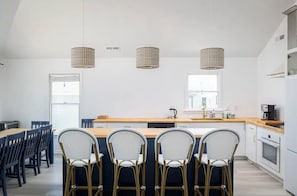 Eine moderne Küche mit einer zentralen Kochinsel, Barhocker, Pendelleuchten und Blick ins Freie.