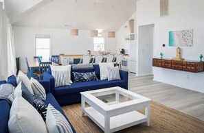 Ein modernes Wohnzimmer mit einem blauen Sofa, einem weißen Couchtisch und einer Küche im Hintergrund.
