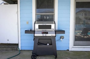 Ein NEEVO Grill für den Außenbereich mit digitaler Anzeige, vor einem blauen Haus mit einer Schiebetür.