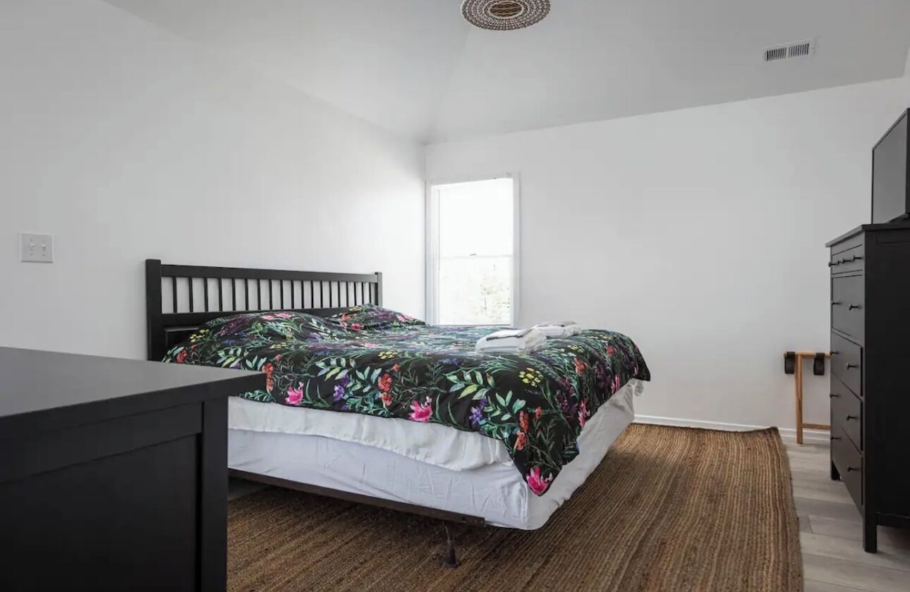 A bedroom with a bed, a dresser, a window, and a ceiling vent.