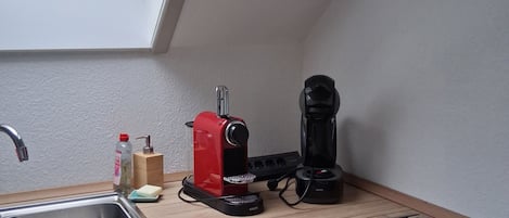 Et køkken med en vask, en rød kaffemaskine, en sort kaffemaskine og et vindue over vasken.