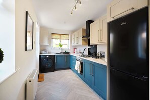 Eine moderne Küche mit einem schwarzen Kühlschrank, blauen Schränken und einem Fenster mit Ausblick.