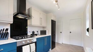 Eine moderne Küche mit Gasherd, Backofen und Mikrowelle, blauen Schränken und einem schwarzen Kühlschrank.