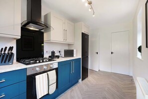 Eine moderne Küche mit Gasherd, Backofen und Mikrowelle, blauen Schränken und einem schwarzen Kühlschrank.