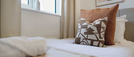 A neatly made bed with white linens and two decorative pillows, one with a geometric pattern and the other with a solid color.