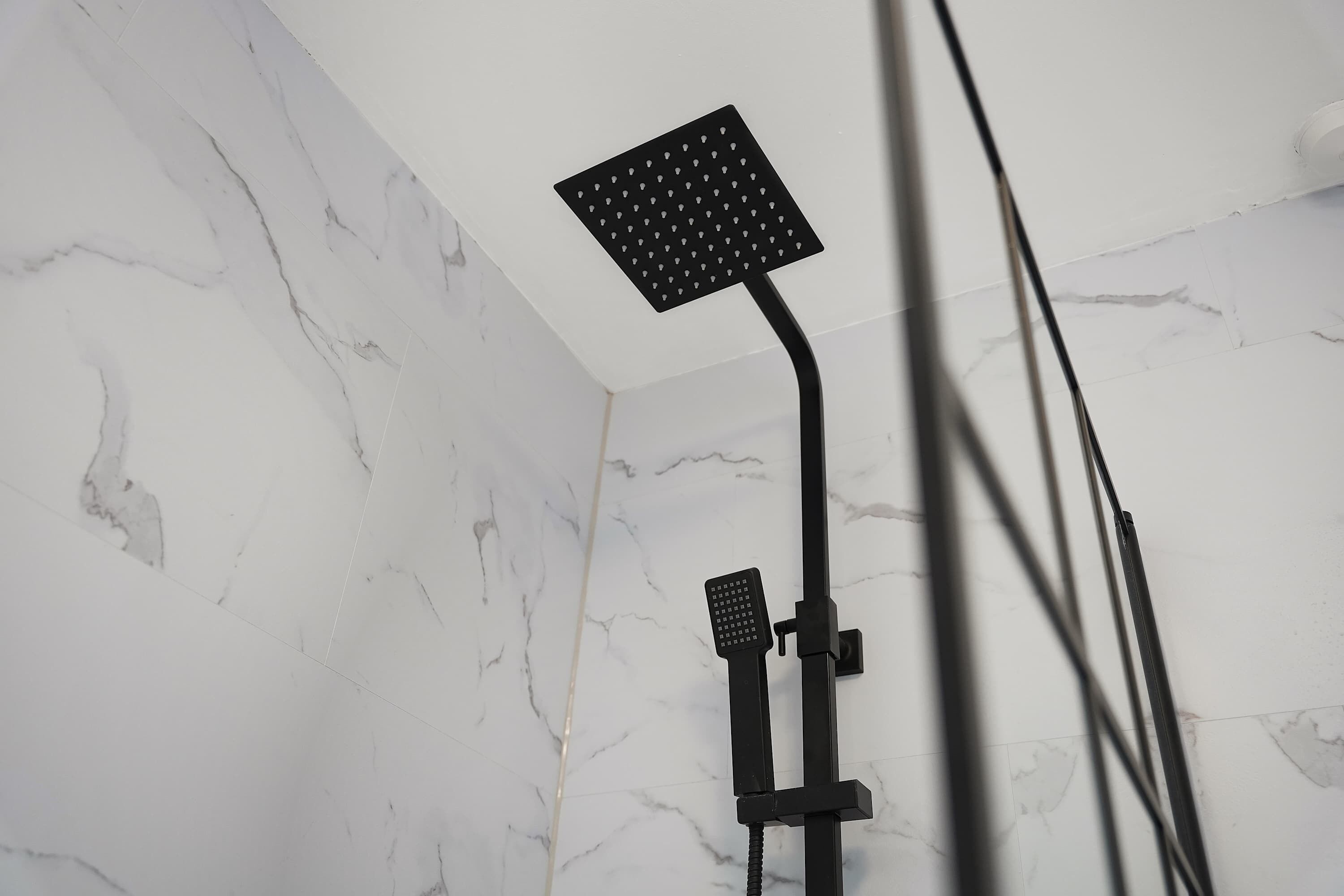A shower with a square head and a handheld showerhead mounted on a black stand.