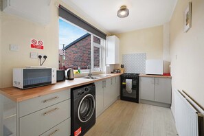 A compact kitchen with a microwave, toaster, sink, and washing machine. - Cozy 3BR Equipped Kitchen By Stay with Us (South Pelaw)