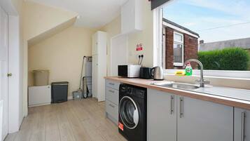 A compact kitchen with a washing machine, a sink, and a window overlooking a brick building.