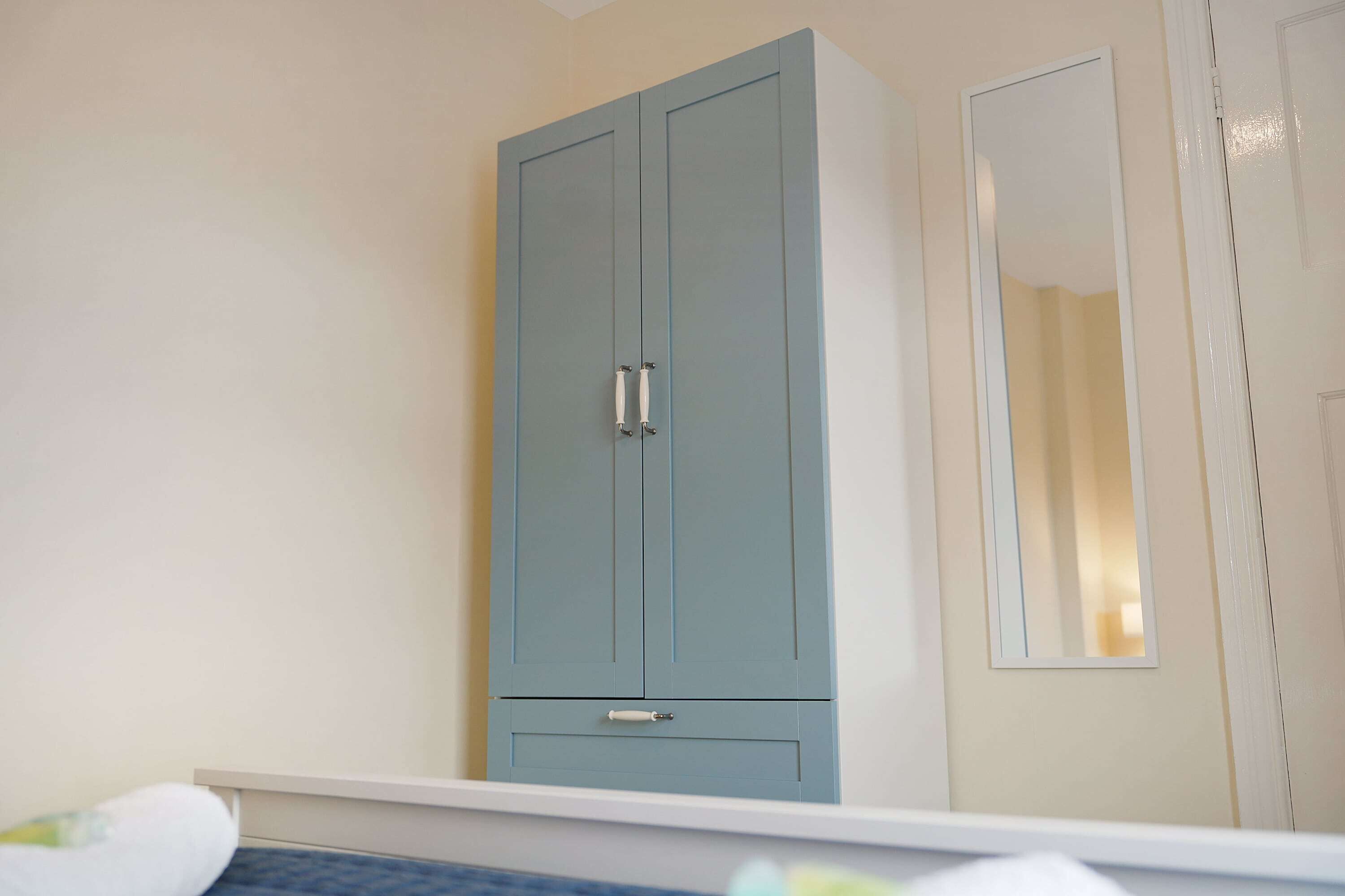 A room with a light blue wardrobe, a white door, and a mirror on the wall.