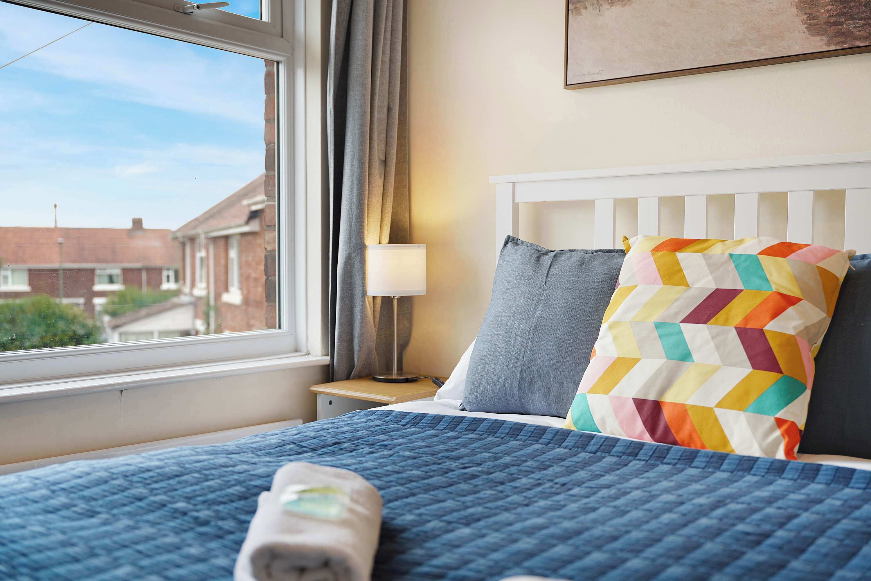 A hotel room with a bed, a window, a nightstand, and a lamp.