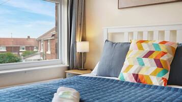 A hotel room with a bed, a window, a nightstand, and a lamp.