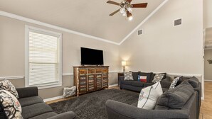 A living room with a ceiling fan, a flat-screen TV, a wooden cabinet, and a grey sofa set. - NEW Stunning River Access, Retreat on Guadalupe River, Tubing, Family Fun Amenities, Tubing Fun (New Braunfels)