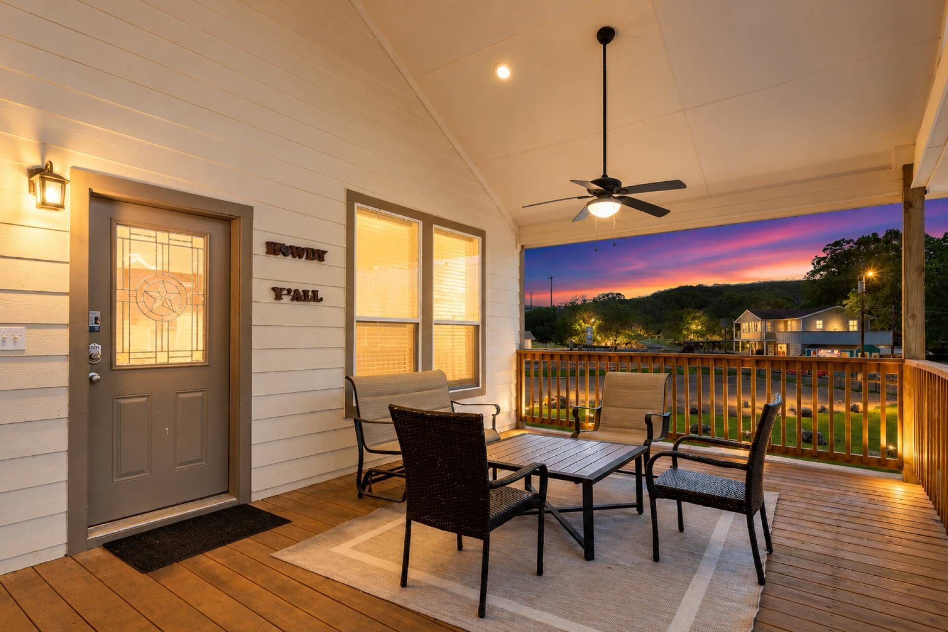 Eine überdachte Veranda mit Deckenventilator, Tisch und Stühlen und Blick auf die Landschaft im Abenddämmerung.