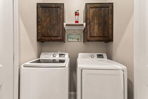 A laundry room with two white front-loading washers and a fire extinguisher on a shelf above them. - NEW Stunning River Access, Retreat on Guadalupe River, Tubing, Family Fun Amenities, Tubing Fun (New Braunfels)