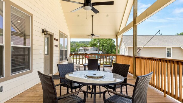 A covered outdoor area with a round table and chairs, a ceiling fan, and a view of houses in the background. - NEW Stunning River Access, Retreat on Guadalupe River, Tubing, Family Fun Amenities, Tubing Fun (New Braunfels)