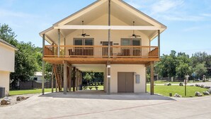 A two-story house with a balcony, a garage door, and a patio area. - NEW Stunning River Access, Retreat on Guadalupe River, Tubing, Family Fun Amenities, Tubing Fun (New Braunfels)