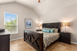 Um quarto com cama, mesas de cabeceira, um criado-mudo, uma janela com persianas e um quadro na parede.